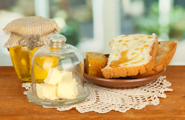 Mantequilla en platillo de vidrio con tapa de vidrio y pan fresco, miel, sobre fondo brillante — Foto de Stock