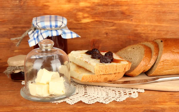 Cam kapak ve taze ekmek ile cam tabak tereyağı, reçel ahşap arka plan üzerinde — Stok fotoğraf