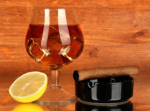 Glass of brandy with ice and lemon on wooden background — Stock Photo, Image