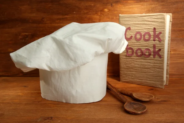 Chef's hat with spoons and cookbook on wooden background — Stock Photo, Image