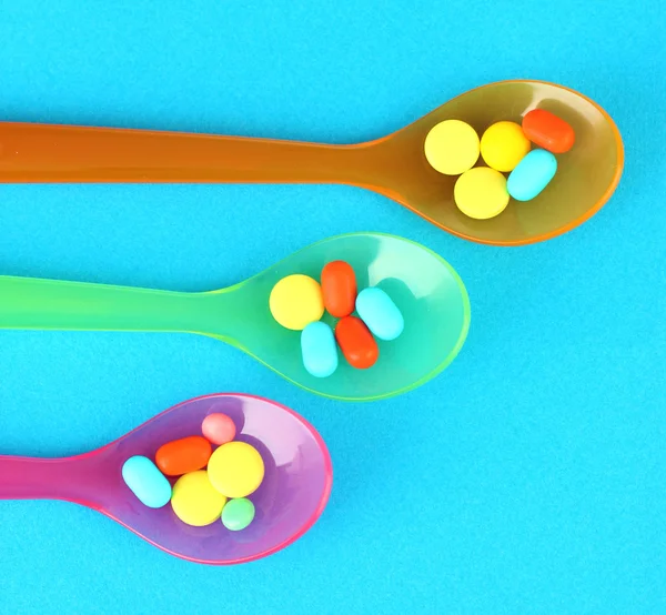 Plastic spoons with color pills on blue background — Stock Photo, Image
