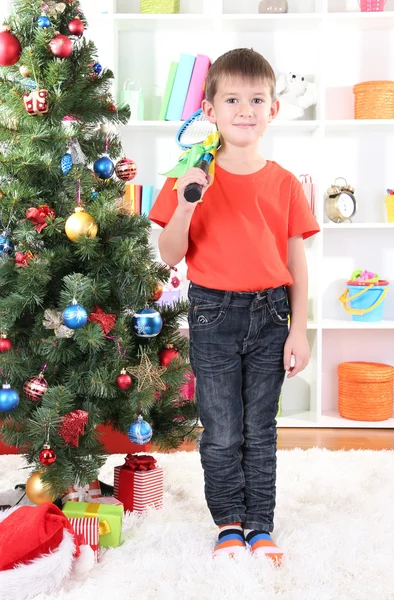Little boy stands near Christmas tree with badminton rackets Royalty Free Stock Images