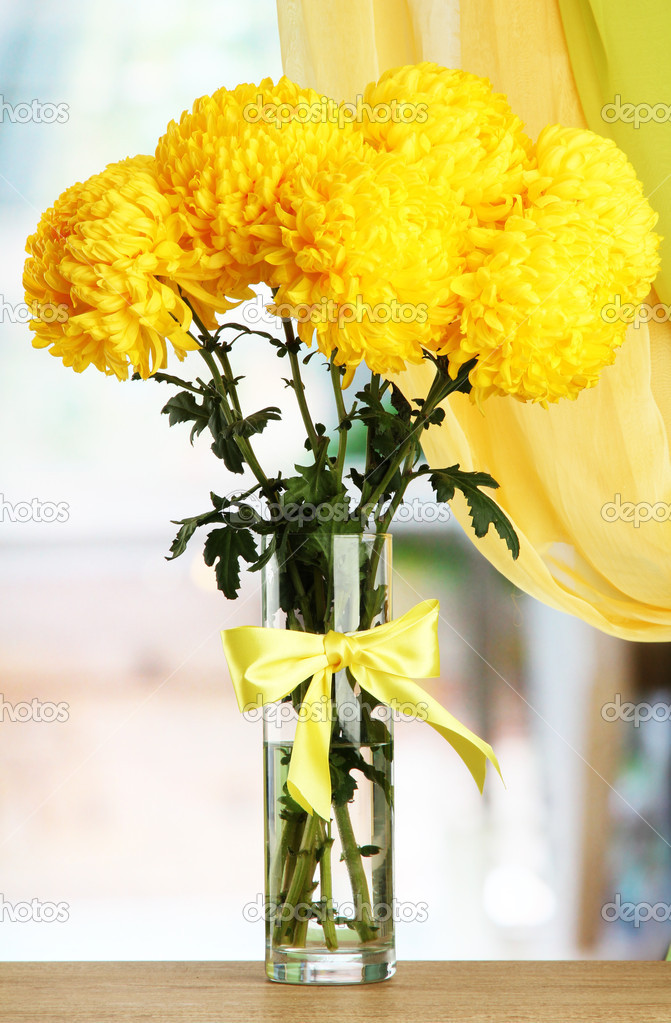 Bright yellow chrysanthemums in glass vase, on wooden table ⬇ Stock