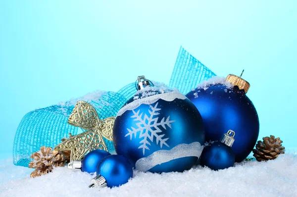 Schöne blaue Weihnachtskugeln und Zapfen im Schnee auf blauem Hintergrund — Stockfoto