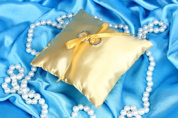 Wedding rings on satin pillow on blue cloth background — Stock Photo, Image