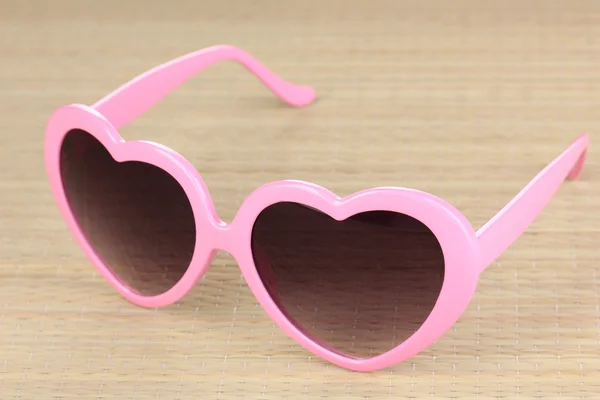 Gafas de sol rosadas en forma de corazón en estera de bambú — Foto de Stock