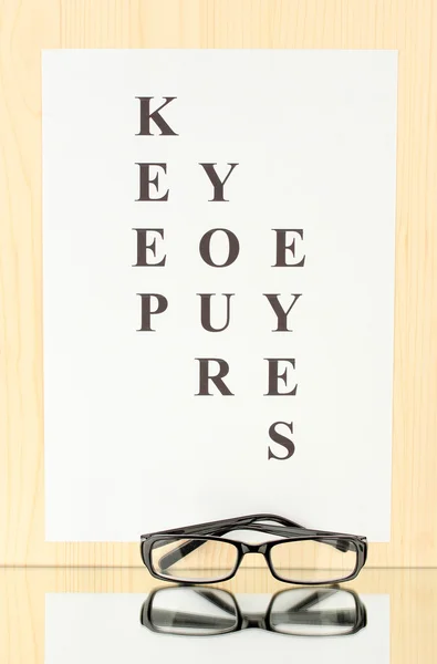 Eyesight test chart with glasses on wooden background close-up — Stock Photo, Image