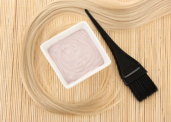 Tintura de cabelo na tigela e escova para coloração de cabelo no tapete de bambu bege, close-up — Fotografia de Stock