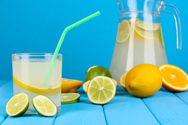 Цитрусовый лимонад в кувшине и стакан цитрусовых вокруг на деревянном столе на голубом фоне — стоковое фото