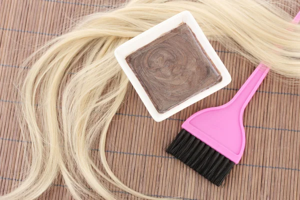 Teinture capillaire dans un bol et une brosse pour colorier les cheveux sur un tapis de bambou brun, gros plan — Photo