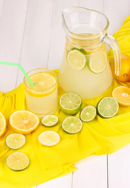 Citrus saft i glas och tillbringare med citrus runt på gult tyg på vita träbord närbild — Stockfoto