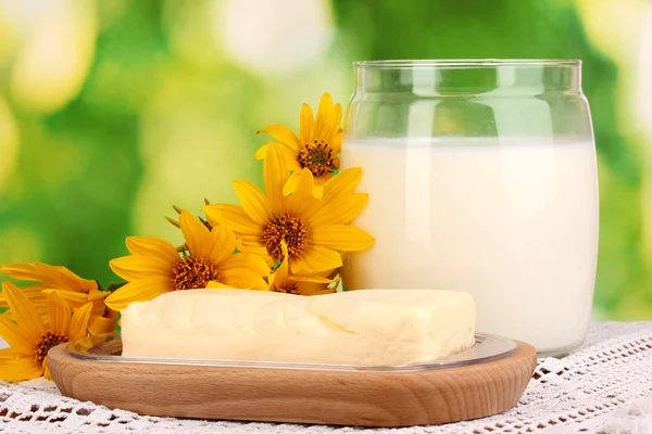Manteiga no suporte de madeira cercado por flores e leite no fundo natural close-up — Fotografia de Stock
