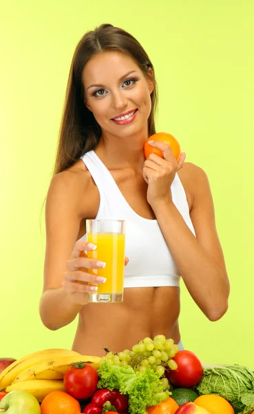 Красива молода жінка з фруктами та овочами та склянкою соку на зеленому фоні — стокове фото