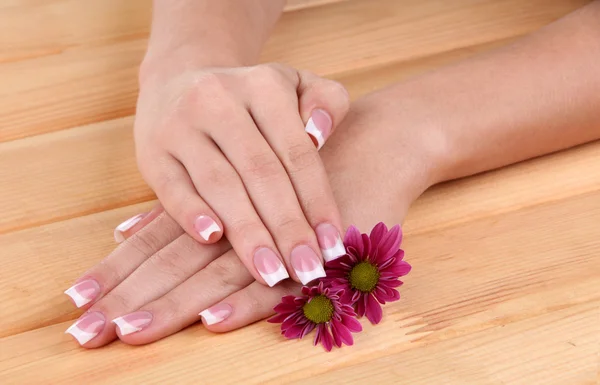 Woman hands with french manicure and flowers on wooden background — Stock Photo, Image