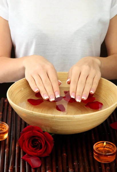 Mãos de mulher com tigela de madeira de água com pétalas — Fotografia de Stock