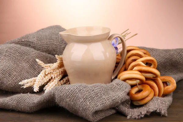 Pot van melk, smakelijke bagels en spikelets op houten tafel, op bruine achtergrond — Stockfoto