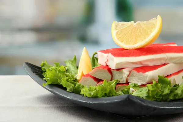 Krabí tyčinky s salát listy a citron na desce, zblízka — Stock fotografie