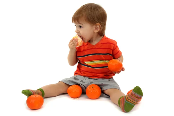 Schattige kleine jongen eten mandarijnen, geïsoleerd op wit — Stockfoto