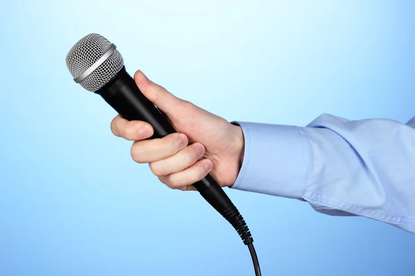 Męskiej ręki mikrofon na niebieskim tle — Zdjęcie stockowe