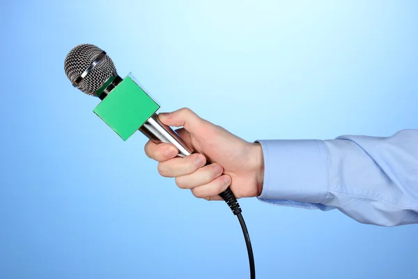 Male hand with microphone on blue background — Stock Photo, Image