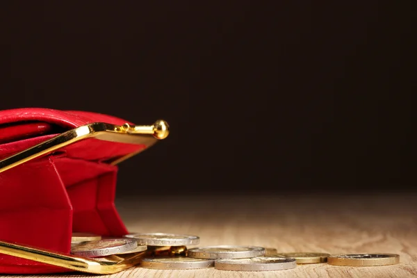 Weibliche rote Brieftasche mit Münzen auf Holztisch, auf schwarzem Hintergrund — Stockfoto