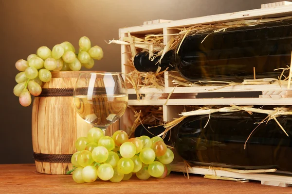 Caixa de madeira com garrafa de vinho, barril, vinho e uva em mesa de madeira sobre fundo marrom — Fotografia de Stock