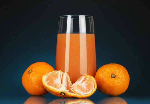 Delicioso suco de tangerina em vidro e mandarinas ao lado dele no fundo azul escuro — Fotografia de Stock