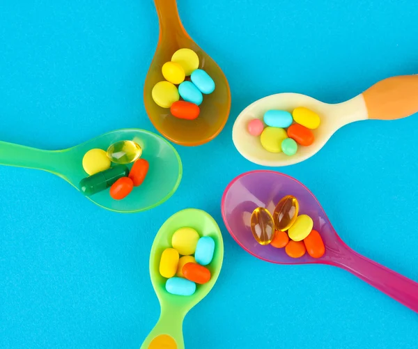 Cucharas de plástico con píldoras de color sobre fondo azul — Foto de Stock