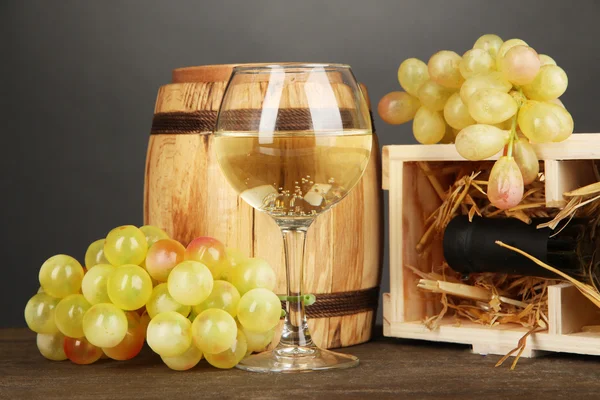 Wooden case with wine bottle, barrel, wineglass and grape on wooden table on grey background Stock Image