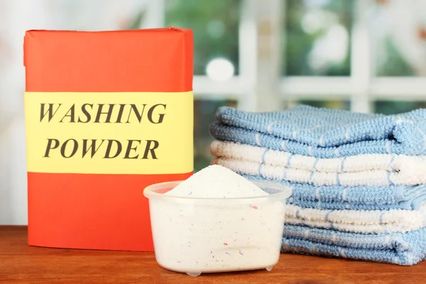 Box of washing powder with blue measuring cup and towels, on wooden table close-up — Stock Photo, Image