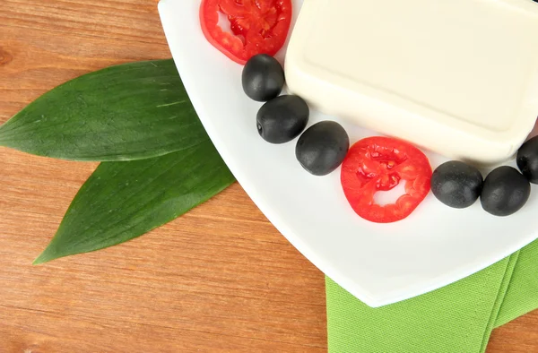 Feta cheese on plate decorated with olives and tomatoes on wooden table close-up — Stock Photo, Image