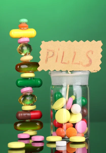 Kapsle a pilulky hill a v nádobě na zeleném pozadí — Stock fotografie