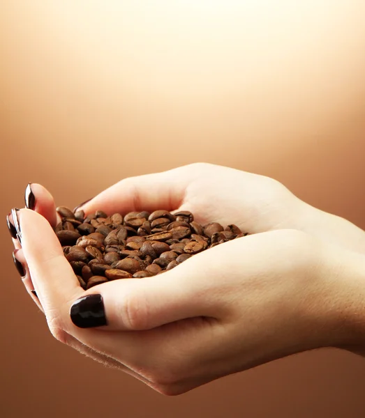 Mani femminili con chicchi di caffè, su sfondo marrone — Foto Stock