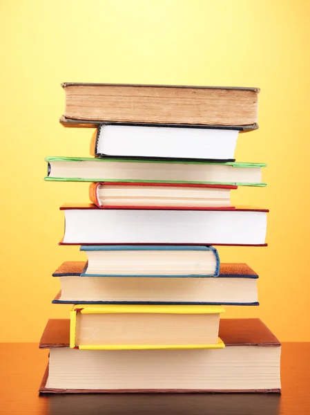 Stack of interesting books and magazines on wooden table on orange background — Stock Photo, Image