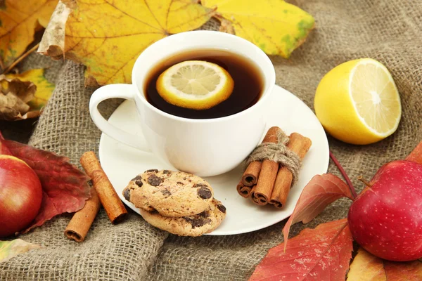 Cup of hot tea and autumn leaves, on burlap background — Stock Photo, Image