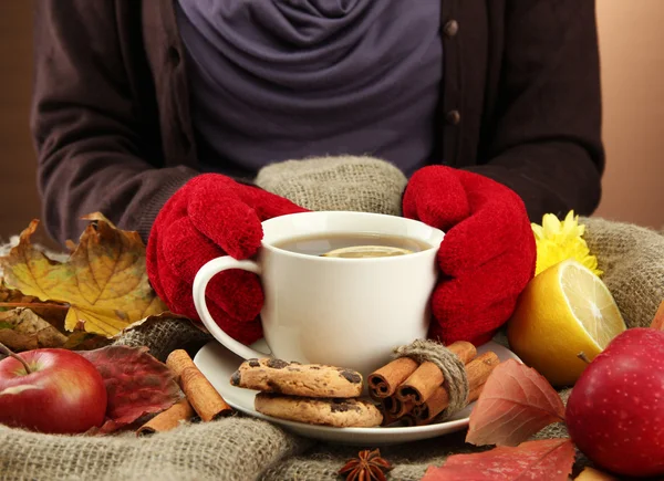 Mains tenant tasse de boisson chaude et feuilles d'automne, sur fond de toile de jute — Photo