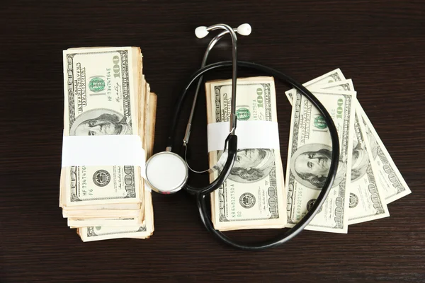 Healthcare cost concept: stethoscope and dollars on wooden background — Stock Photo, Image