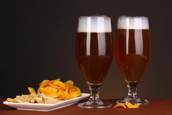 Glazen bier met chips en crackers geïsoleerd op bruine achtergrond — Stockfoto