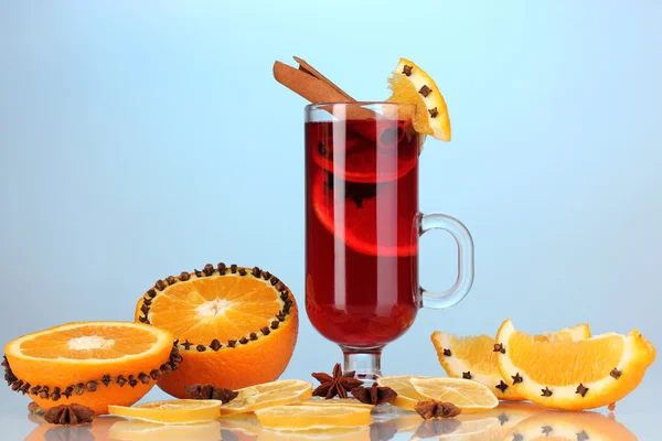 Fragrant mulled wine in glass with spices and oranges around on blue background — Stock Photo, Image