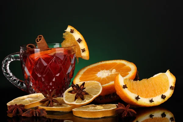 Duftender Glühwein im Glas mit Gewürzen und Orangen auf grünem Hintergrund — Stockfoto