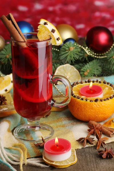 Fragrant mulled wine in glass with spices and oranges around on wooden table on red background — Stock Photo, Image