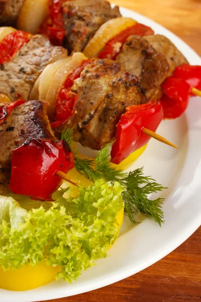 Carne grelhada saborosa e verduras no espeto na chapa, na mesa de madeira — Fotografia de Stock