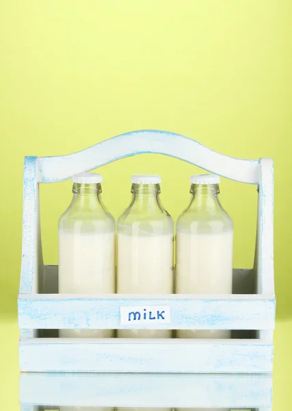 Milk in bottles in wooden box on green background — Stock Photo, Image