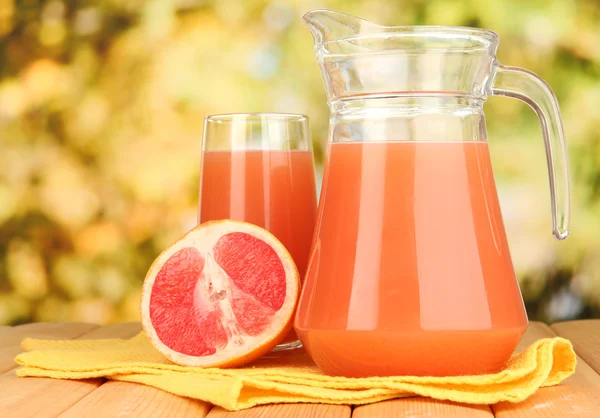 Full glass and jug of grapefruit juice and grapefruits on wooden table outdoor — Stock Photo, Image