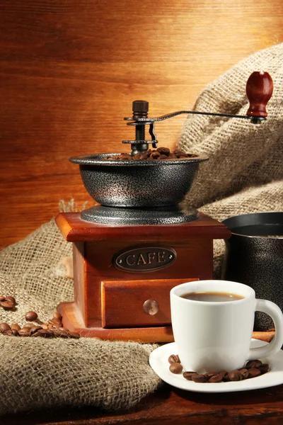 Coffee grinder, turk and cup of coffee on brown wooden background — Stock Photo, Image