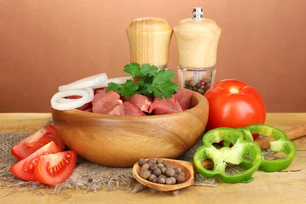 Сырое мясо говядины с травами и специями на деревянном столе на коричневом фоне — стоковое фото