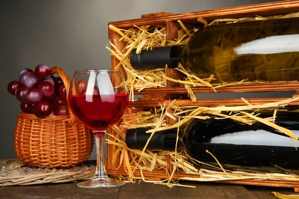 Holzkoffer mit Weinflaschen, Weinglas und Trauben auf Holztisch auf grauem Hintergrund — Stockfoto