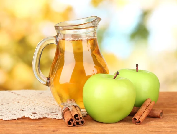 Jarra llena de zumo de manzana y manzana sobre mesa de madera sobre fondo brillante — Foto de Stock