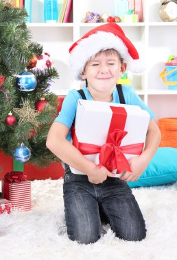 Noel Baba şapkalı küçük çocuk elinde hediye yılbaşı ağacının yanında oturur