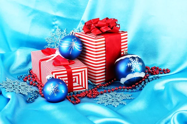 Kék karácsonyi labdák, hópelyhek és gyöngyök a kék háttér színes piros ajándékok — Stock Fotó